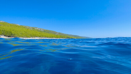 Tranquil blue water of Adriatic Sea and lush coastline overgrown with pine trees. Clear sky and...