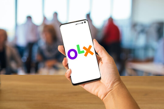 hand holding cell phone with the Olx logo and blurred people in the background, Rio de Janeiro, Brazil, May 2024