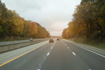 Driving through a scenic autumn highway, with trees in fall colors lining the open road under a soft sunset.