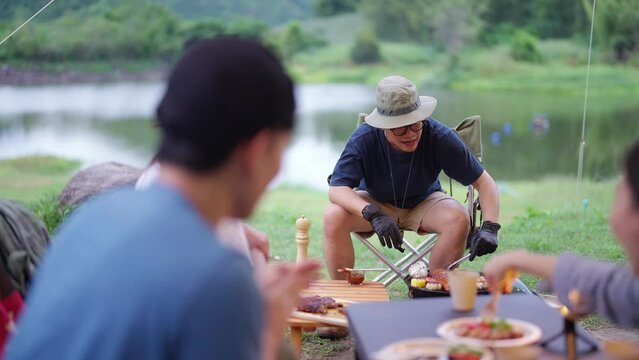 Group of Happy Asian man and woman enjoy and fun outdoor lifestyle travel nature camping in forest on summer vacation. People friends having dinner eating bbq grill and drinking beer together at night