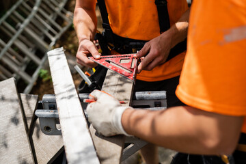 Two construction workers using a carpenter square to measure angles for a precise cut on a wooden board