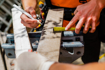 Construction worker measuring a wooden board with a tape measure, preparing for an accurate cut