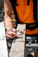 Construction worker marking a wooden board with a pencil, preparing it for precise cutting
