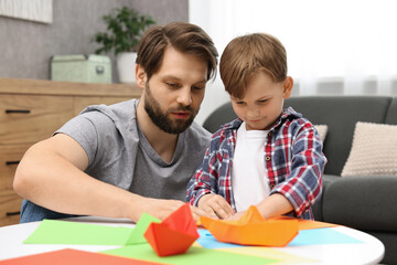 Dad and son making paper boats at coffee table indoors