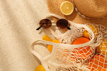 String bag with sunglasses, straw hat and fruits on beige textured background, flat lay. Space for...