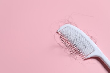 Comb with lost hair on pink background, space for text