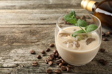 Coffee cream liqueur in glass, beans and mint on wooden table, closeup. Space for text
