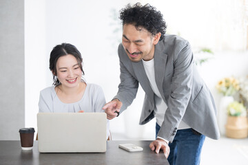 Bosses teaching subordinates in front of computers with a smile, men and women in office casuals,...