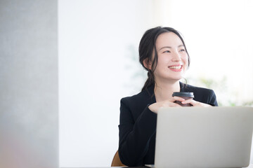 woman looking up holding coffee and using computer in office Bright image of job change, hiring, etc. Copy space on the right