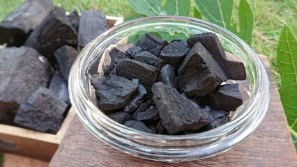 Charcoals in glass bowl on wooden background.