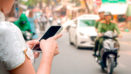 Woman using phone in a street with Vietnamese police officers ride motorcycles.
