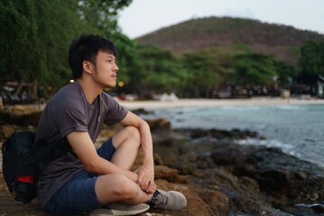 asian man sitting on the rock looking toward the sea