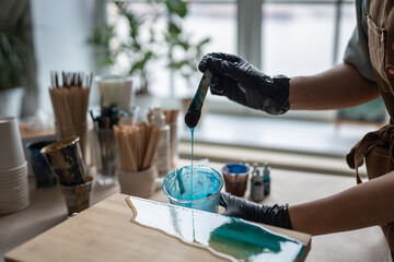 Female artist pours epoxy resin on wooden board. Craftswoman using liquid art technique, creating...