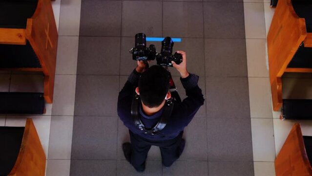 overhead shot of videographer in back long sleeve shirt using double black leather strap with dual cameras, raising the both simultaneously to record at wedding 60fps