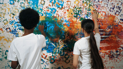 Back view of young diverse children paint colorful stained wall with hand. Attractive highschool...