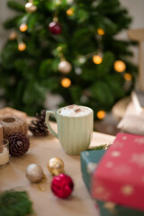 Cup of hot chocolate with marshmallow and christmas ornaments on wooden table near christmas tree while preparing decoration for celebrate christmas festive holiday and winter seasons at home