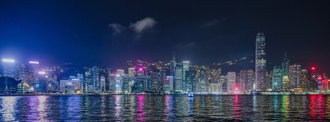 Panorama of Hong Kong City skyline with tourist sailboat at night. View from across Victoria Harbor...