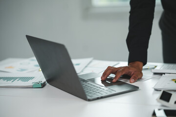 Business professional working on a laptop at a modern office desk with documents and charts, emphasizing productivity and technology.