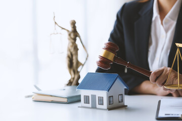 Lawyer holding gavel near model house and justice scale, symbolizing real estate law and property...