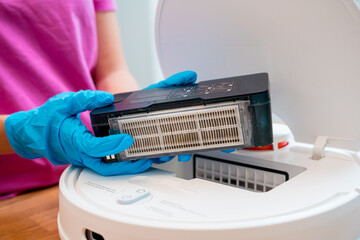 A young woman cleans a robot vacuum cleaner from dirt after cleaning.