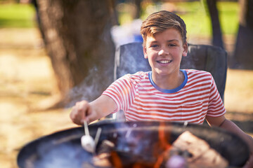 Boy, campfire and marshmallow for roasting, smile and happiness outside in nature. Camper, sunshine...