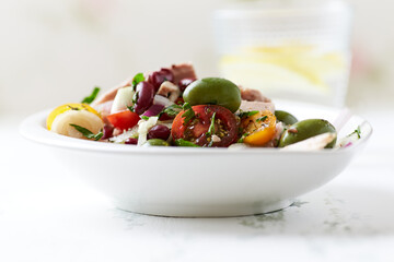 Salad with tuna, green olives and cherry tomatoes. Bright wooden background. Close up. Copy space.