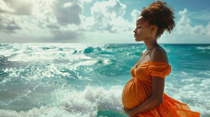 Pregnant woman in orange dress standing on the beach and looking at sea