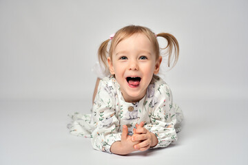 Portrait of little girl with blue eyes and blond hair wearing white dress. Cute child laying on a...