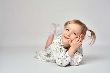 Portrait of little girl with blue eyes and blond hair wearing white dress. Cute child laying on a...