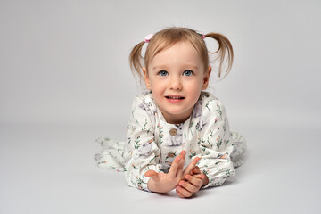 Portrait of little girl with blue eyes and blond hair wearing white dress. Cute child laying on a white background