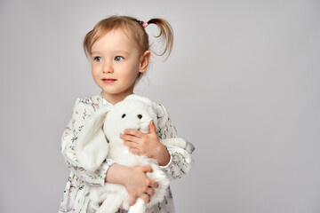 Little girl with white bunny on a white background with copy space. Portrait of beautiful little girl hugging her rabbit toy