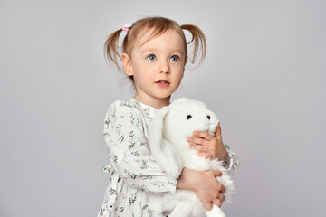 Little girl with white bunny on a white background with copy space. Portrait of beautiful little girl hugging her rabbit toy