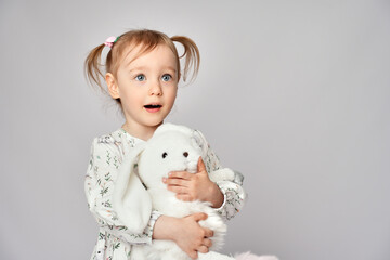Little girl with white bunny on a white background with copy space. Portrait of beautiful little girl hugging her rabbit toy