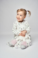 Little girl with white bunny on a white background with copy space. Portrait of beautiful little girl hugging her rabbit toy