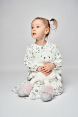 Little girl with white bunny on a white background with copy space. Portrait of beautiful little girl hugging her rabbit toy