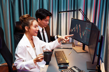 Smiling businesswoman in white suit pointing on dynamic stock exchange statistic on pc screens...