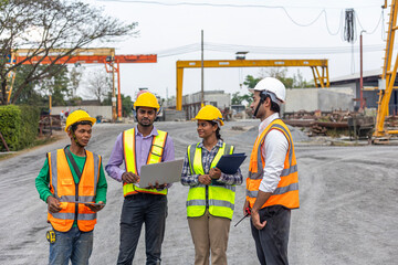 A team of civil engineers with safety uniform from different ethnicities work together using laptop and digital devices to inspect their production in a construction factory.