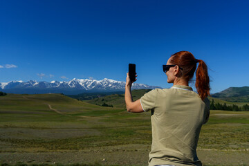 mature woman traveling stopped by the side of the road and takes pictures of the mountains on her phone