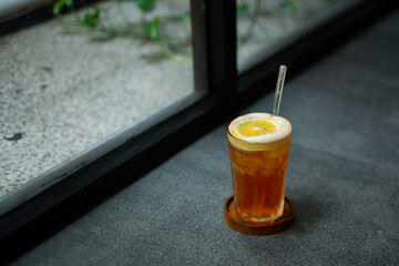 iced lemon tea drink served on transparent glass over small wooden plate on stone tile