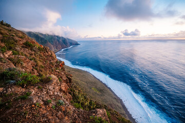 Fototapeta premium View of rough ocean with waves, volcanic beach, sunset over a huge cliff in Lighthouse Ponta do Pargo, Madeira, Portugal