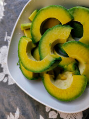 A bowl of fresh avocado slices. Avocados have many benefits such as maintaining heart and eye health and more. Vegetarian food and also for dieting. Deep black background with white floral patterns.