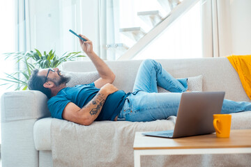 One man chilling and relaxing laying on the sofa at home using mobile phone to watch funny online...