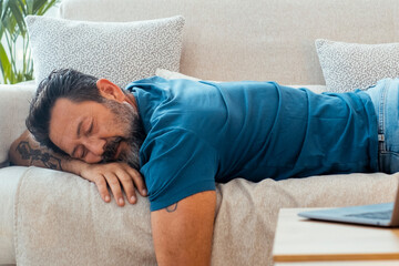 One man fall asleep at home for afternoon nap laying on the sofa with open laptop on the table....