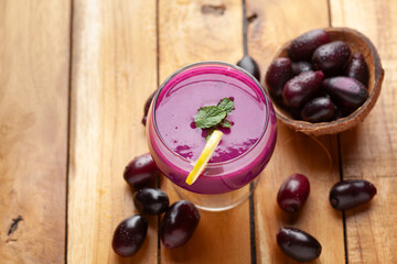 A glass of 'Indian blackberry' or Jamun (Syzygium cumini) Shake, Pulp, or Juice with the whole fresh fruits, on a wooden background.