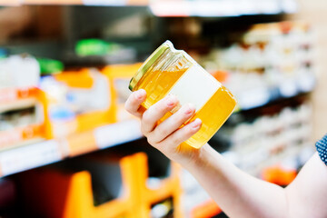 Young male hand holds honey on a blurred background, a row of shelves with groceries in supermarket