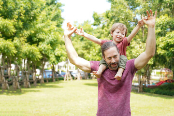 Obraz premium Happy Family. Happy little boy stretching out hands while his father carrying him cheerful and enjoying in the garden park. Father and boy relax and chill outdoor on summer day