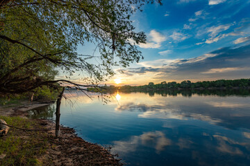 As the spring sun dips below the horizon, its golden light creates a dreamy glow over the peaceful waters of the lake.