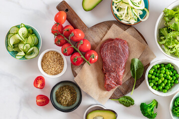 Set of aw ingredients to cooking a healthy plate on on a marble background, beef tenderloin, bulgur grains and various vegetables top view, diet food, copy space