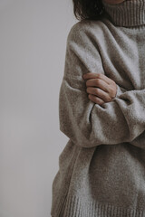 Closeup view of pretty young woman wearing warm knitted sweater pullover over white wall. Aesthetic fashion vogue composition. Neutral pastel color