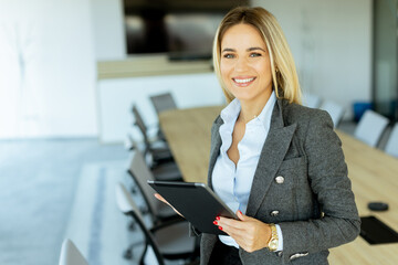 Smiling professional woman in red blazer holding tablet in modern conference room during daytime